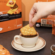 Biscuit coréen Ace au caramel salé Haitai trempé dans une tasse de café, avec emballages du produit en arrière-plan.