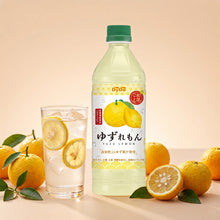 Bouteille 500ml de boisson japonaise DyDo Yuzu Citron avec un verre glacé, des tranches de citron et des yuzus frais sur fond doux.