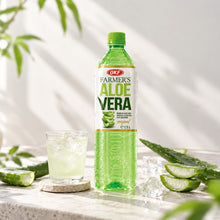 Boisson à l’aloe vera OKF Farmer’s Original 1,5 L, bouteille verte accompagnée de morceaux d’aloe vera et d’un verre frais avec glaçons.