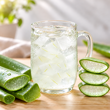 Boisson glacée à l’aloe vera avec morceaux d’aloe dans un verre à anse, accompagnée de feuilles d’aloe vera fraîches