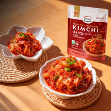 Kimchi extra piquant Jongga servi dans deux bols blancs sur une table en bois, avec son sachet de 80 g en arrière-plan.