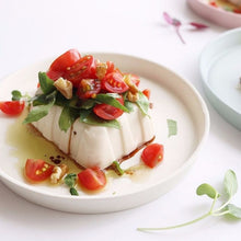 Tofu moelleux moulé en forme cannelée, garni de tomates cerises coupées, feuilles vertes et morceaux de noix, arrosé d’une sauce huile d’olive et vinaigre balsamique, présenté sur une assiette blanche minimaliste – ACEMARTmall Paris