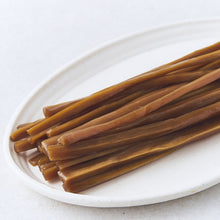 Racines marinées coréennes brunâtres coupées en longues lamelles, légèrement brillantes, disposées sur une assiette blanche – ACEMARTmall Paris