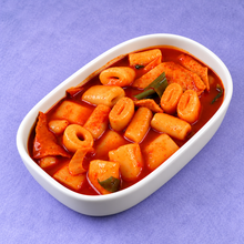 Galettes de riz coréennes en tubes creux pour tteokbokki, nappées d’une sauce rouge épicée avec des morceaux de pâte de riz et de légumes dans un plat blanc.