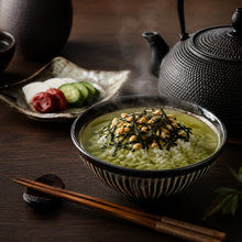 Bol d’ochazuke japonais au riz, thé vert et algues nori, servi avec des pickles, des baguettes et une théière en fonte sur une table sombre.