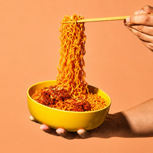 Bol de ramen coréen carbonara épicée Korean Street, avec nouilles relevées soulevées aux baguettes sur fond pêche.