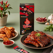 Sauce piquante coréenne Buldak Original Samyang en sticks, servie avec des ailes de poulet et des travers de porc grillés.
