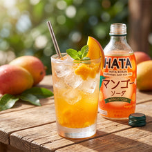 Verre de soda à la mangue pétillant Hatakosen servi avec garniture de fruits et bouteille à côté.