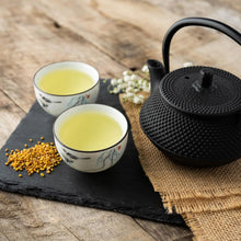 Sobacha japonais au sarrasin torréfié servi chaud dans deux tasses, avec théière en fonte noire et grains de sarrasin sur une table en bois.