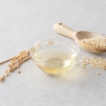 Bol en verre contenant un liquide clair à base de riz, avec grains de riz et épis en arrière-plan - ACEMARTmall Paris
